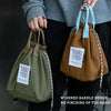 A person holds a brown waterproof insulated lunch bag with a light blue drawstring and a green one.