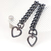 A dark metal heart-shaped chain extender is displayed against a clear, ribbed background.