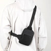 A black canvas crossbody sling bag worn by a person in a white hooded jacket.