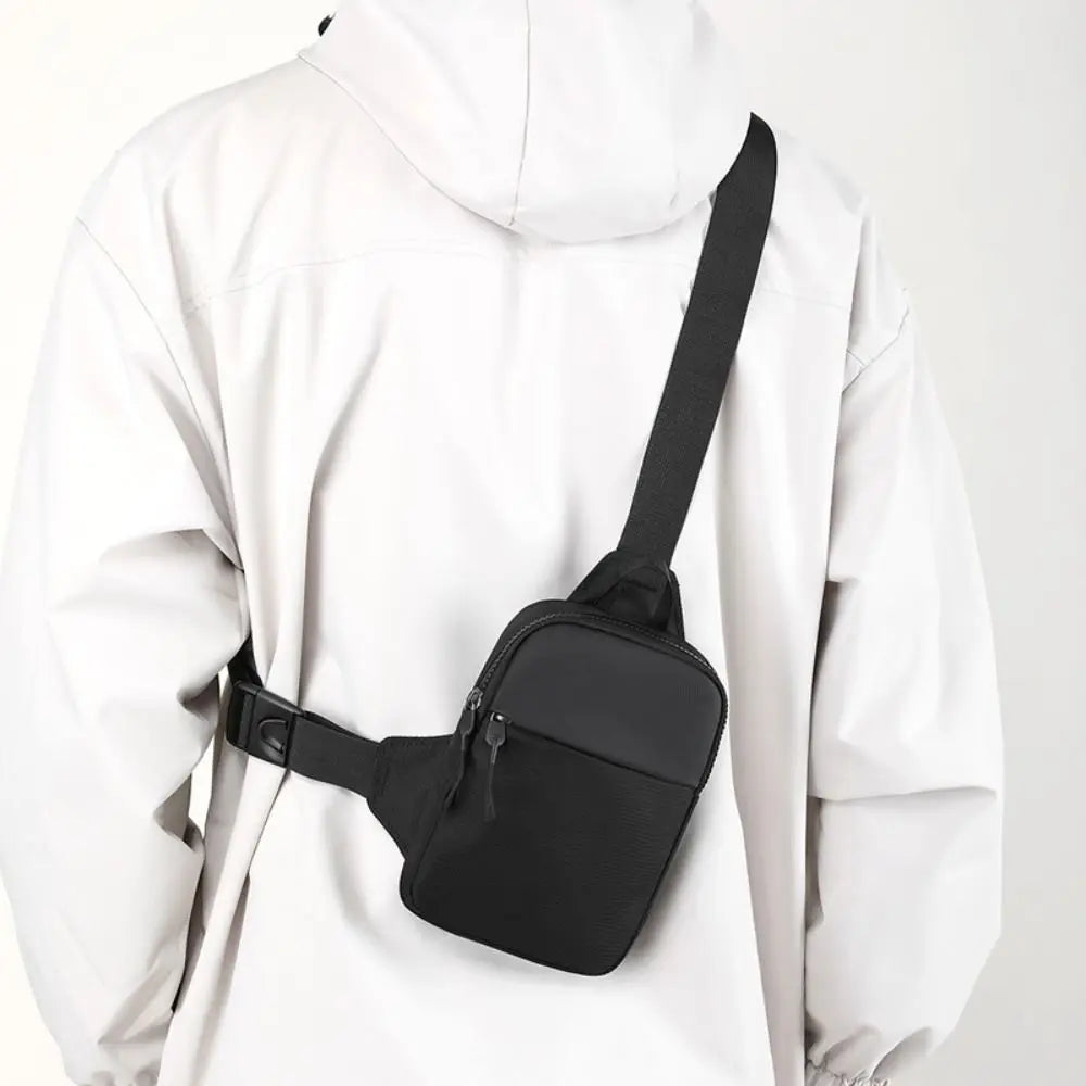A black canvas crossbody sling bag worn by a person in a white hooded jacket.