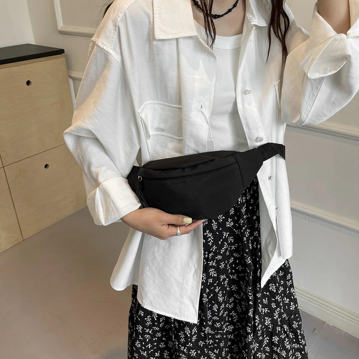 A person wearing a white shirt and jacket holds a black nylon crossbody sling bag.