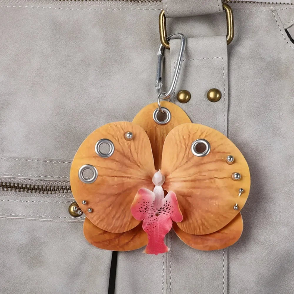 A realistic peach-colored phalaenopsis orchid flower keychain attached to a light gray leather bag.