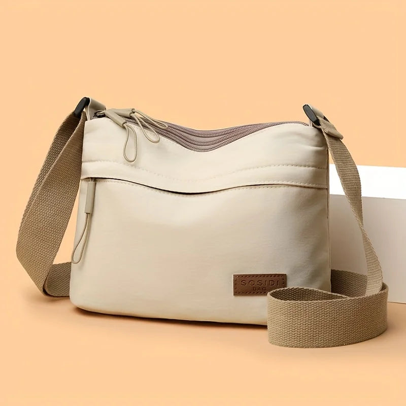 A beige nylon crossbody shoulder bag with multiple zippered compartments shown against a light background.