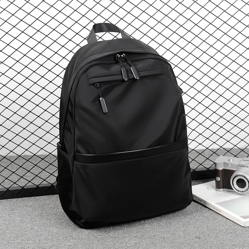 A black men's lightweight laptop backpack is shown against a wire mesh background.