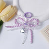 A purple and clear pearl bowknot keychain with a silver heart charm resting on a white surface next to a yellow rose.