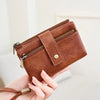 A brown leather wallet with a zipper closure and brass hardware is held in a person's hand.