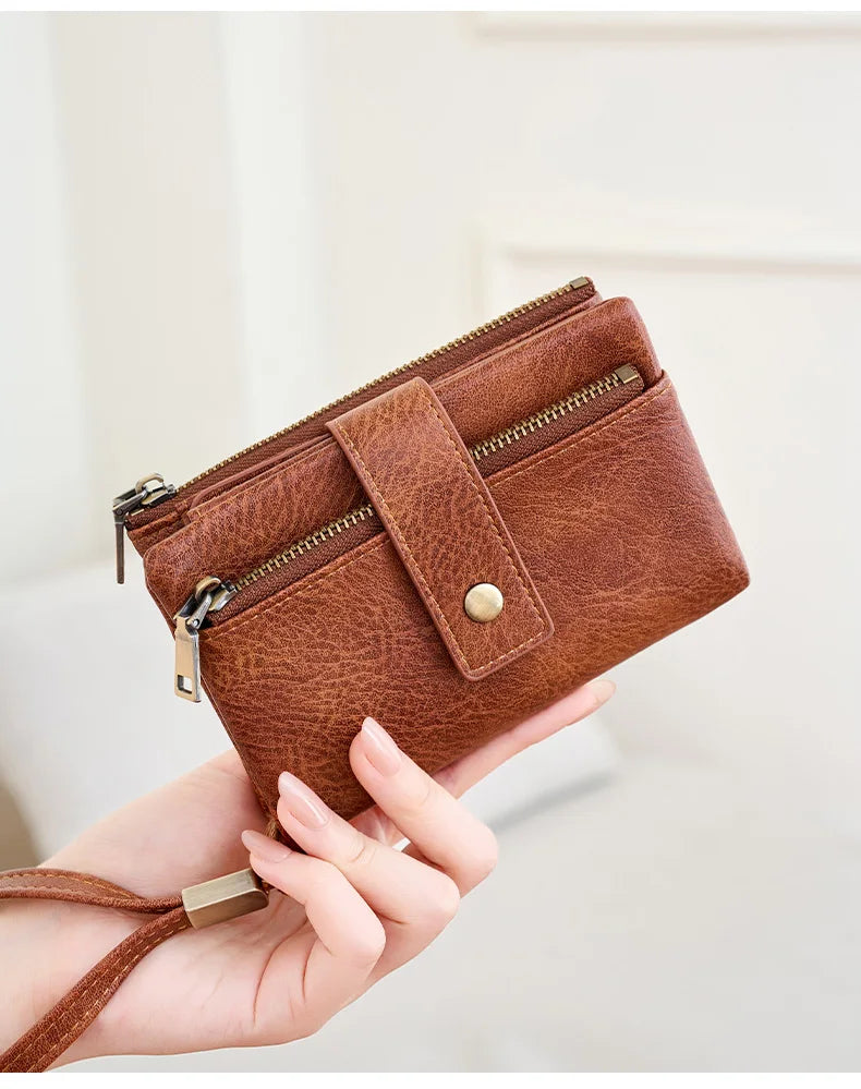 A brown leather wallet with a zipper closure and brass hardware is held in a person's hand.