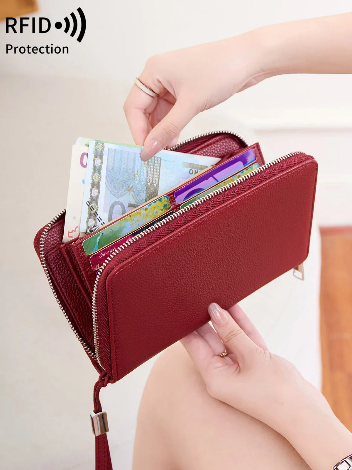 A hand is opening a maroon PU leather zipper wallet to show various credit cards and cash inside.