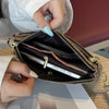 A hand is opening a brown zippered wallet to reveal a silver credit card and some paper inside.