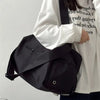 A black canvas crossbody travel tote bag carried by a person wearing a white shirt.