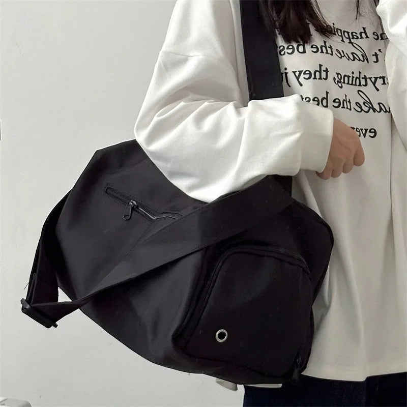 A black canvas crossbody travel tote bag carried by a person wearing a white shirt.