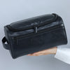 Schwarze Vintage-PU-Leder-Toiletten-Tasche mit Reißverschluss und Aufhänger, in der Hand gehalten.