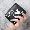 A hand holds a black leather mini zipper coin purse featuring a white Hello Kitty design on the front.