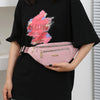 Une femme tient une pochette banane waterproof rose avec un design abstrait scintillant sur un t-shirt noir.