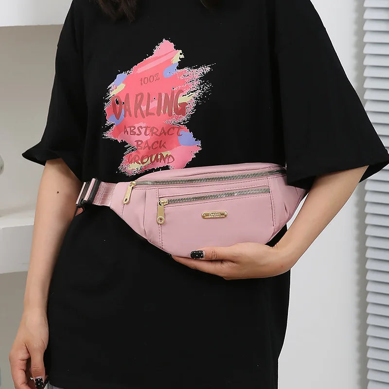 Une femme tient une pochette banane waterproof rose avec un design abstrait scintillant sur un t-shirt noir.