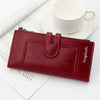A maroon leather wallet with a zipper and flap is shown next to a white cup on a light background.
