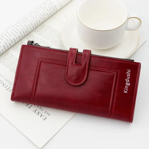 A maroon leather wallet with a zipper and flap is shown next to a white cup on a light background.