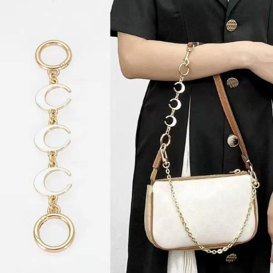 A white moon-shaped bag chain strap with a gold alloy clasp is shown against a black garment.