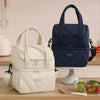 Una bolsa de almuerzo aislada blanca reutilizable junto a una azul marino sobre una mesa de madera.