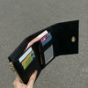 A black card holder wallet is shown open, displaying various cards and cash, held by a hand.
