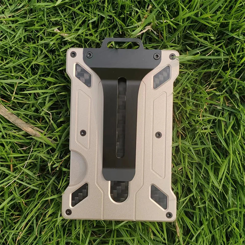 A slim aluminum metal ID card wallet with a matte beige finish and black accents resting on green grass.