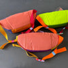 A collection of colorful patchwork color block fanny packs in orange, pink, and lime green.