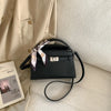 A black PU leather crossbody clutch bag with light pink and white striped fabric detail resting on a cream-colored garment.