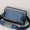 A dark blue leather crossbody bag with a gray strap is shown against a light background.