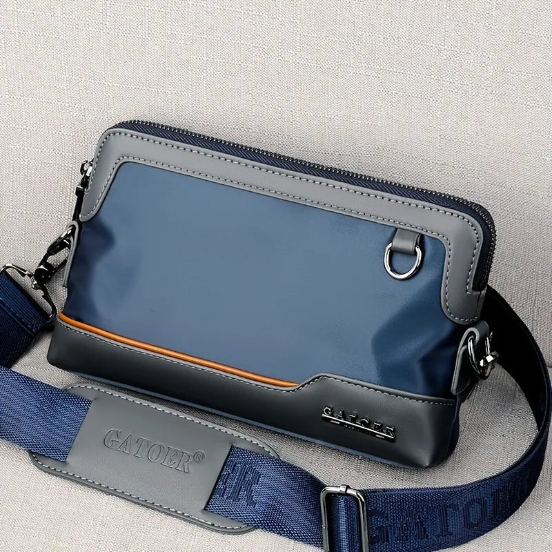 A dark blue leather crossbody bag with a gray strap is shown against a light background.
