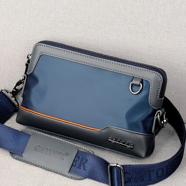 A dark blue leather crossbody bag with a gray strap is shown against a light background.