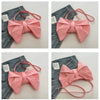 A pink pleated bow crossbody tote bag is shown against a denim background.