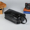 Black men's PU leather clutch handbag lying on a gray surface next to a camera and wooden box.