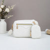 Weiße gesteppte Crossbodytasche mit goldfarbenen Details auf weißem Untergrund neben getrockneten Blumen.