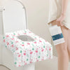 A white disposable toilet seat cover is shown placed on a toilet, with a folded white cover in a hand nearby.