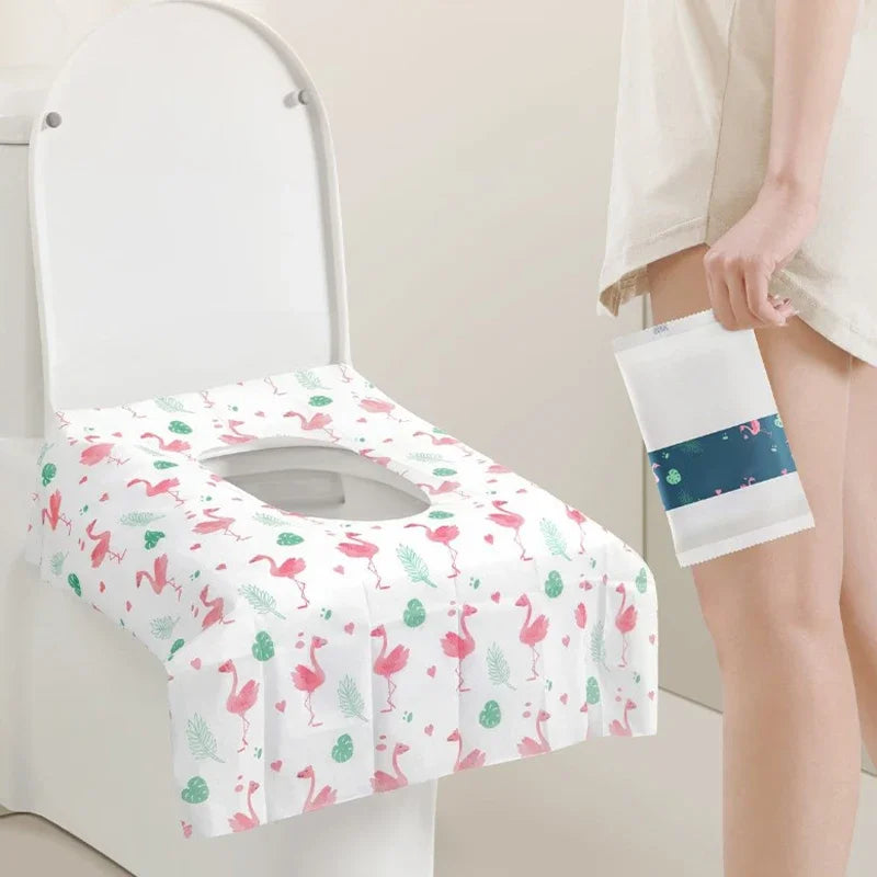 A white disposable toilet seat cover is shown placed on a toilet, with a folded white cover in a hand nearby.