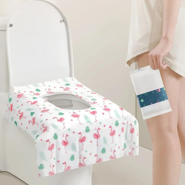 A white disposable toilet seat cover is shown placed on a toilet, with a folded white cover in a hand nearby.