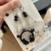 Silver and black music headphone keychain and phone strap displayed on a white card.