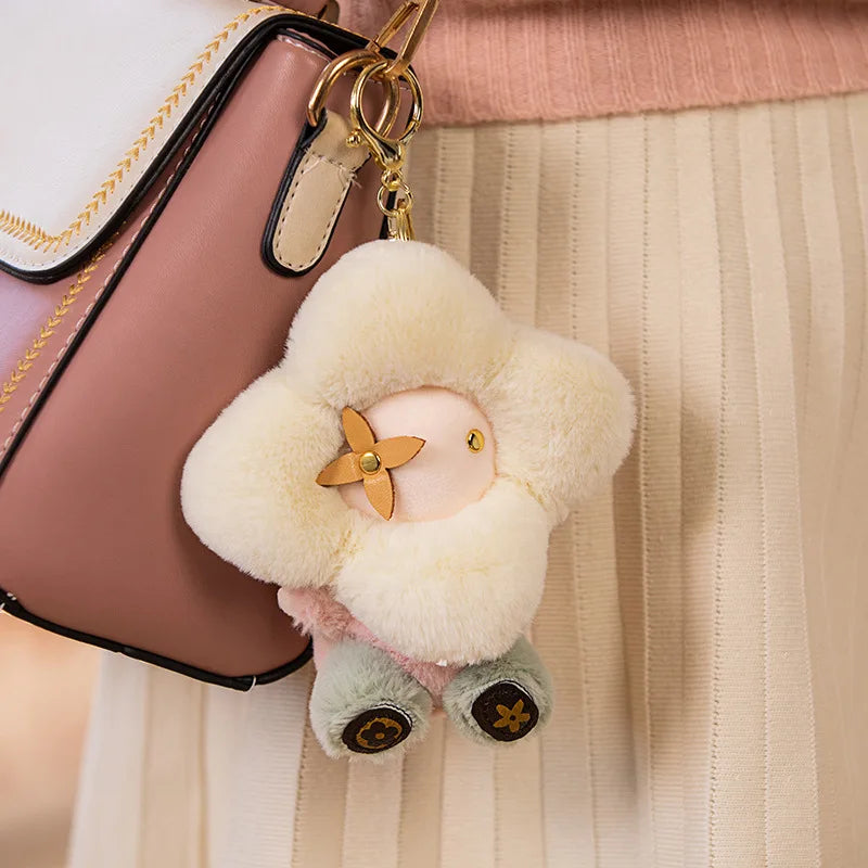 A cute sunflower plush keychain with yellow petals and green accents hanging from a pink leather bag.
