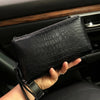 Un bolso de mano con estampado de cocodrilo negro sostenido en la mano de una persona dentro del interior de un coche.