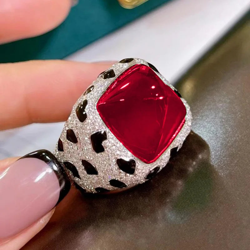 A close-up of a luxury leopard crystal statement ring featuring a red gemstone set in a silver-toned, leopard-print crystal h