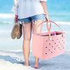 A person holds a pink waterproof beach bag organizer with dividers on a sandy beach.