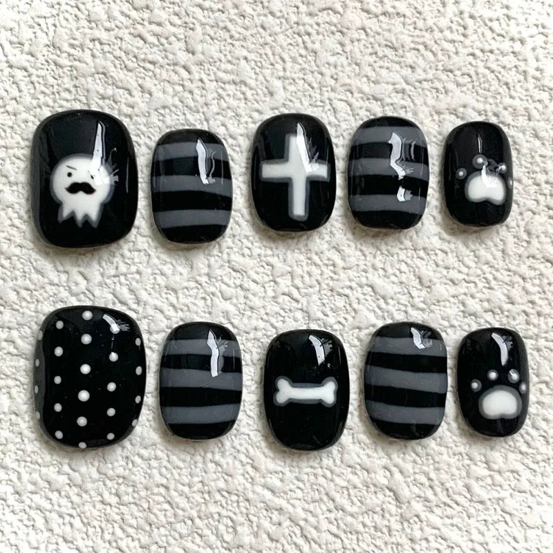 A set of press-on nails featuring various black and white designs including a ghost, cross, and bone.