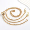 Cartera de metal dorado con cadena y cierre de percebe, junto a una esfera decorativa, sobre fondo blanco.
