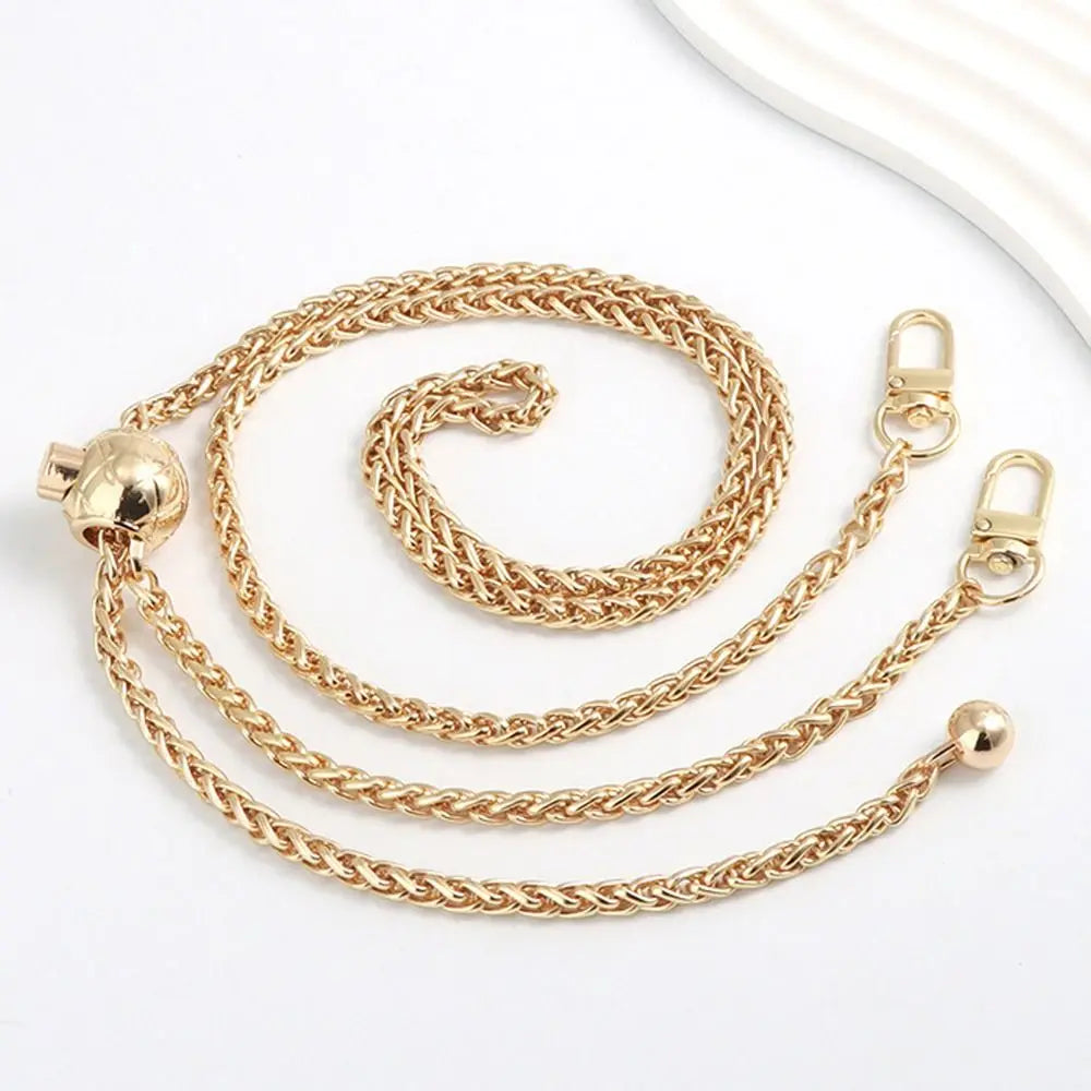 Cartera de metal dorado con cadena y cierre de percebe, junto a una esfera decorativa, sobre fondo blanco.
