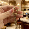A hand holds a gold-toned metal strap extender chain with a loop and a link, displayed in a well-lit interior setting.