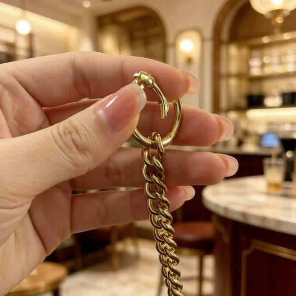 A hand holds a gold-toned metal strap extender chain with a loop and a link, displayed in a well-lit interior setting.