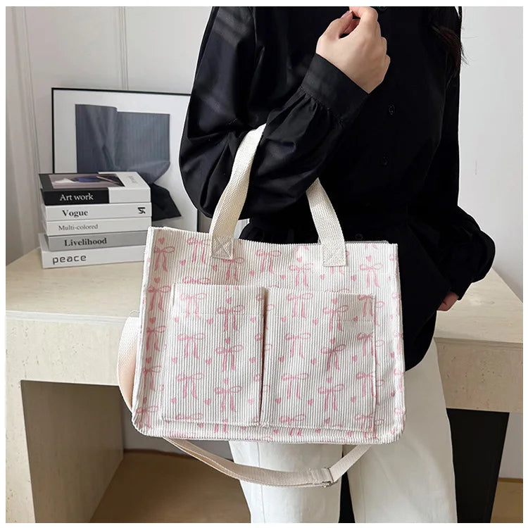 A white canvas tote bag with a pink strawberry pattern is held by a person against a light background.