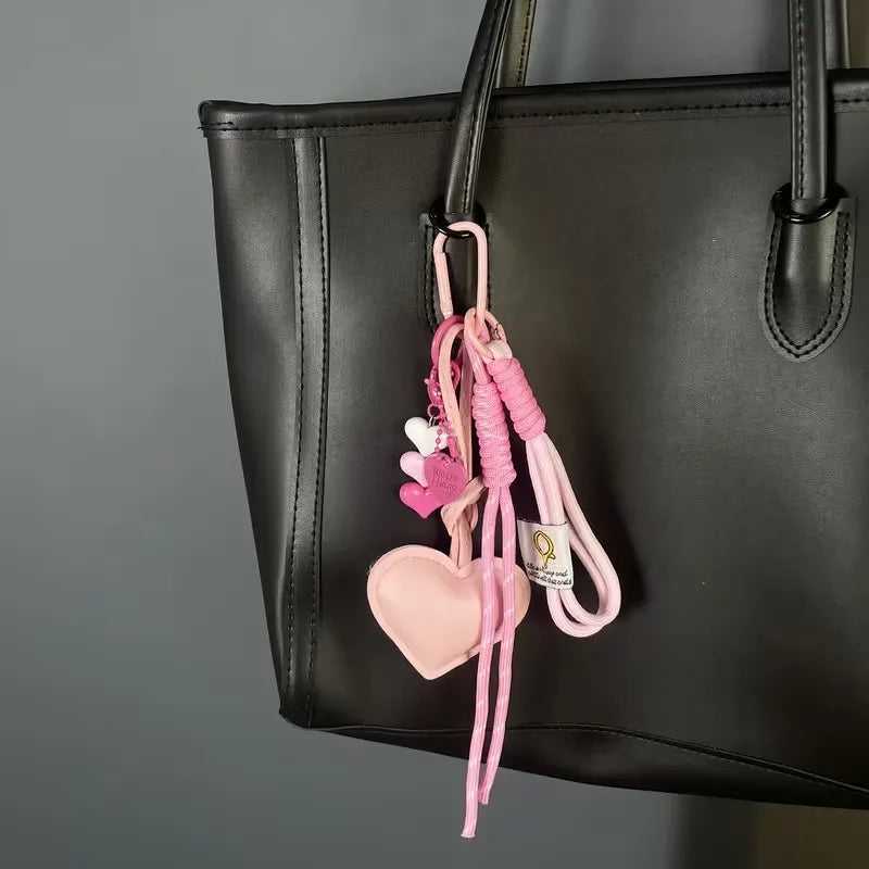 A black leather handbag with a pink heart keychain featuring braided pink rope and a small heart charm.