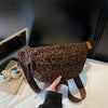 A brown leopard print crossbody bag with a leather strap is being held by a hand on a white surface.
