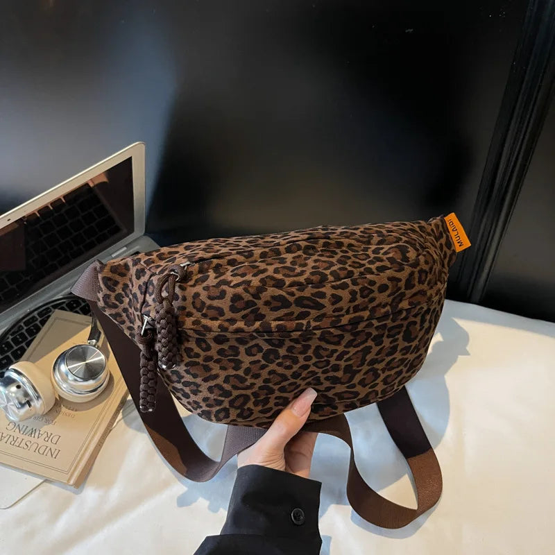 A brown leopard print crossbody bag with a leather strap is being held by a hand on a white surface.